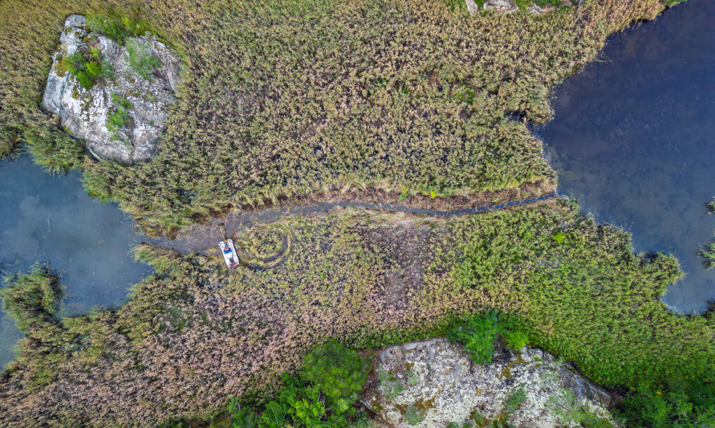 En grävmaskin gräver en kanal mellan två vattenområden.